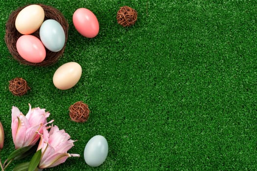 Colorful Easter eggs in the nest with pink lily flower on a lawn grass background.