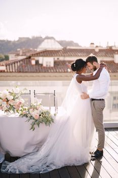 Interracial wedding couple. Destination fine-art wedding in Florence, Italy. African-American bride and Caucasian groom stand near the table for wedding dinner