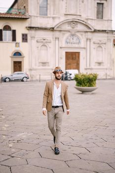 A young guy with a straw hat, a white unbuttoned shirt and a sand jacket, a small beard walks around of Florence.