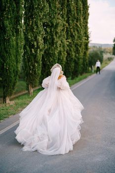 Wedding at an old winery villa in Tuscany, Italy. The bride runs on the way to the groom. A row of cypresses along the road.