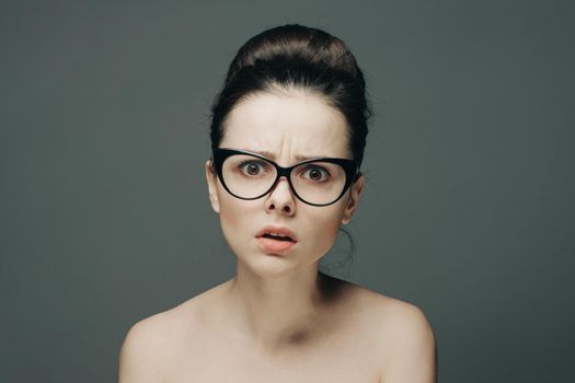 woman with glasses naked shoulders gathered hair gray background. High quality photo