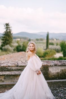 The bride in a white lush dress, with bare shoulders and puffed sleeves, walks on the roof of an old villa. Wedding at an old winery villa in Tuscany, Italy.