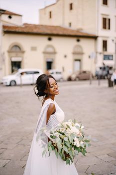 African-American bride in white dress and long veil. With a lush bouquet of the bride in her hands. Wedding in Florence, Italy.