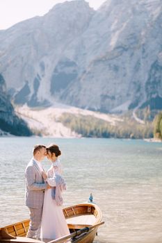 Bride and groom sailing in wooden boat, with oars at Lago di Braies lake in Italy. Wedding in Europe - Newlyweds are standing embracing in boat