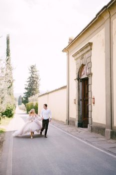 Beautiful bride and groom running hand in hand outside of the old villa in Italy, in Tuscany, near Florence.