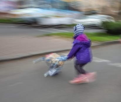 Little girl with toy stroller crossing the road.  Intentional motion blur