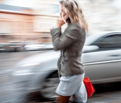 Abstract image of a young woman talking on a mobile phone on a city background with car. Intentional motion blur