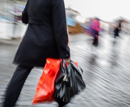 Abstract image of a woman walking down the street in the rain with a red package and black bag. 