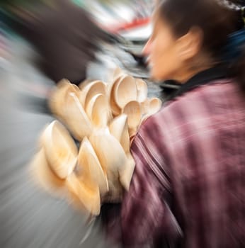 Young woman holding a lot of wooden spoons for sale. Intentional motion blur