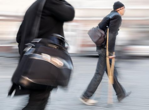 Businessman with a briefcase and a man on crutches walk along a city street. Intentional motion blur