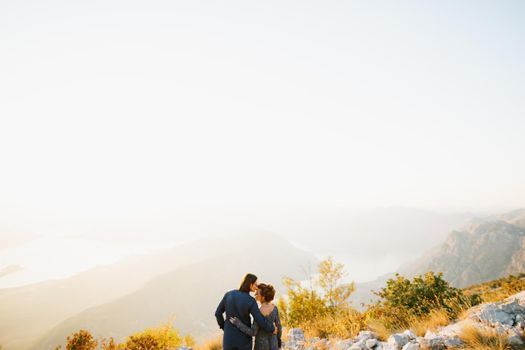 The bride and groom embracing and kissing on the Lovcen mountain behind them opens a view of the Bay of Kotor, back view . High quality photo