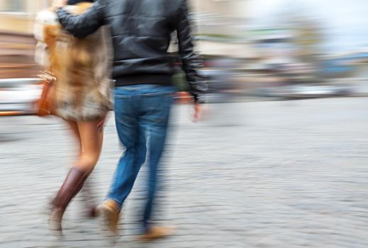 Man in jeans and a woman in a fur coat walking down the street hugging. Intentional motion blur