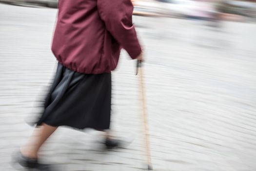 Elderly sick woman with a cane walking down the street. Intentional motion blur