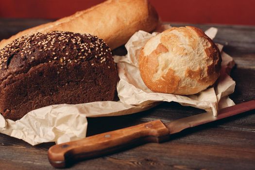 loaf of rye bread and flour products on paper packaging knife on a wooden table and red background. High quality photo