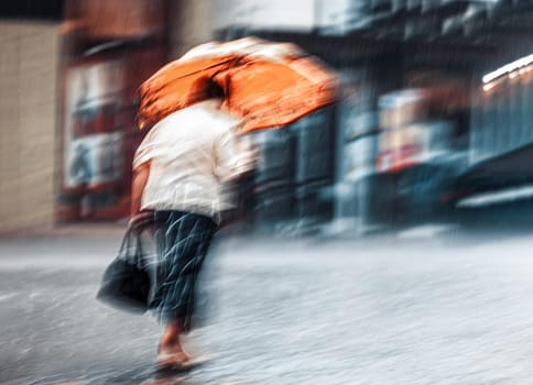 Intentional motion blur image with lonely woman with orange umbrella walking down the street in rainy day. 