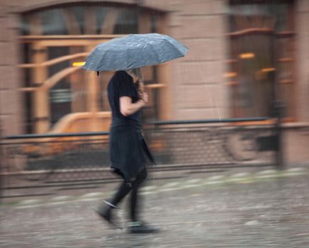 Shower. Woman walking down the street in rainy day. Intentional motion blur