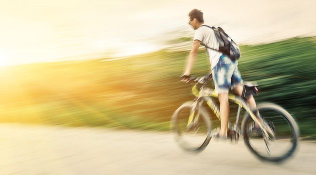 Boy cyclist in traffic on the city roadway in sun light. Intentional motion blur and color shift