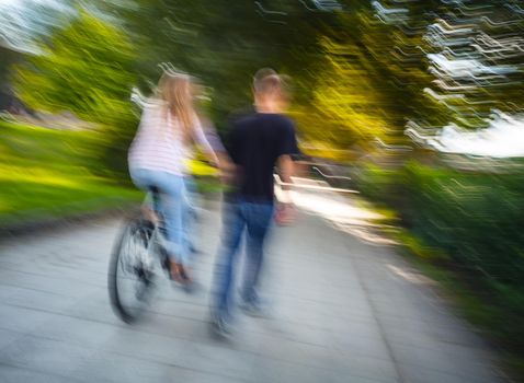 Young man and woman on a bicycle going through the autumn alley.  Intentional motion blur