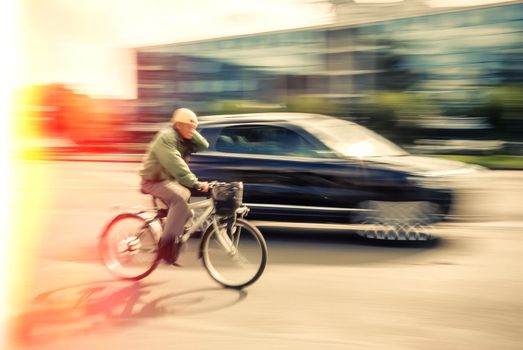 Cyclist and a car on the street. People hurrying about their business. Image in motion blur style. Cross Process stylization. 