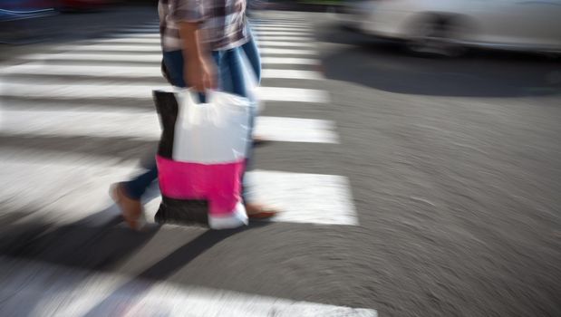 Woman with shopping bag crossing the street at a crosswalk. Intentional motion blur