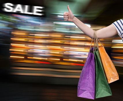 Sale. Hand with shopping bags against blurred mall on the background with copy-space