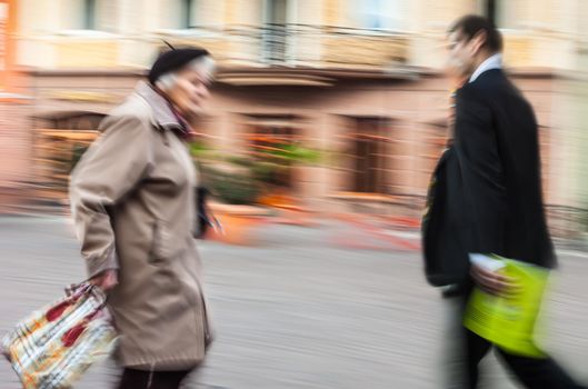 Old age and youth concept. An elderly woman walks down the street to meet a business young man in a suit.  Intentional motion blur