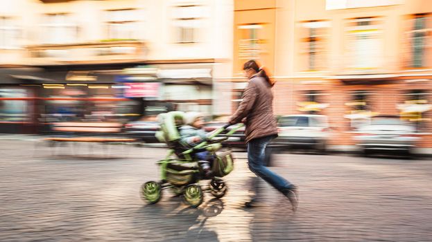 Mother with small children and a pram walking down the street. Intentional motion blur