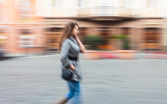 Abstract image of a young woman talking on a mobile phone on a city background with car. Intentional motion blur
