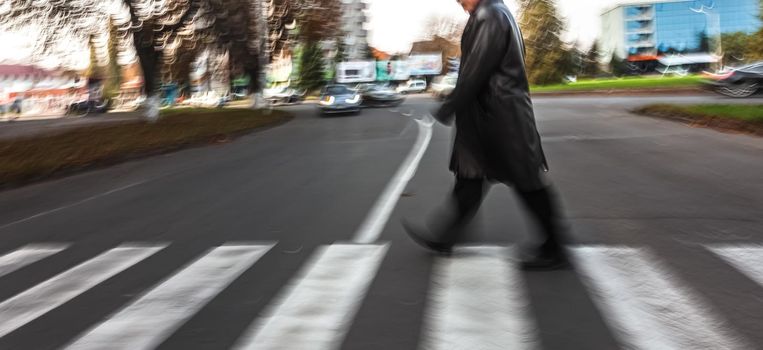 An elderly man crosses the street in a crosswalk. Intentional motion blur