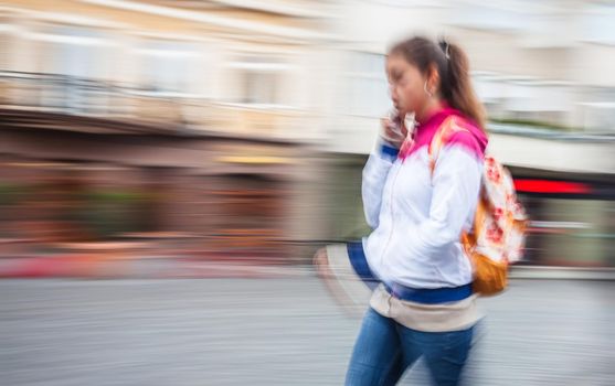 Abstract image of a young woman talking on a cell phone in a hurry. Intentional motion blur