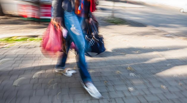 Young woman with bags and packages on the road in the city. Intentional motion blur