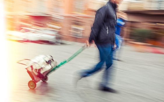 Middle-aged man carries the cart with bag. Intentional motion blur