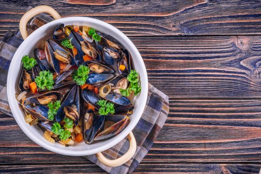 Boiled mussels in cooking dish with parsley on dark wooden background