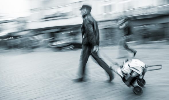 Middle-aged man carries the cart with bag. Intentional motion blur