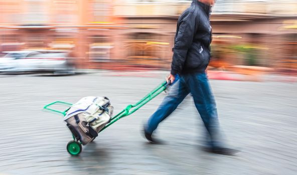 Middle-aged man carries the cart with bag. Intentional motion blur