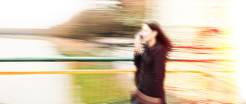 Abstract image of a young woman talking on a cell phone in a hurry. Intentional motion blur