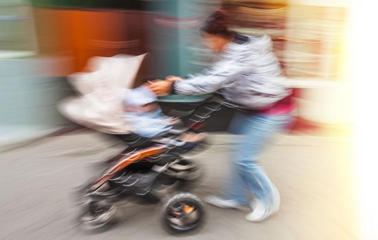 Mother with small children and a pram walking down the street. Intentional motion blur