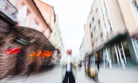 Elderly gray-haired man with a mobile phone on the street of the old city. Intentional motion blur