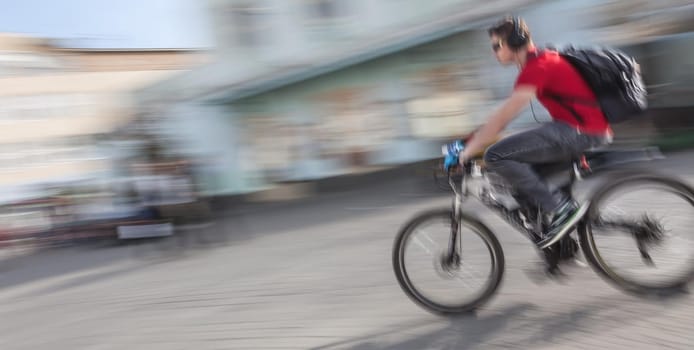 Young man with headphones and backpack riding a bicycle on the street. Intentional motion blur