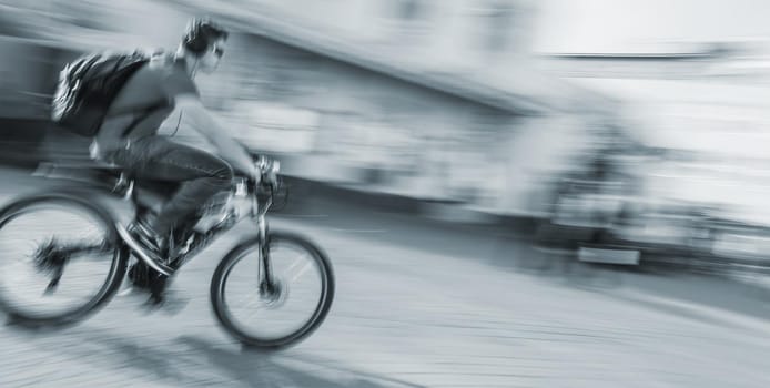 Young man with headphones and backpack riding a bicycle on the street. Intentional motion blur