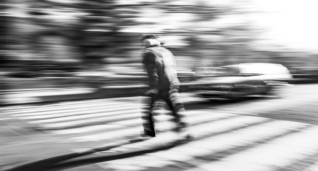 Dangerous situation on zebra crossing. Black and white image of an elderly man runs across the road in front of the car. Intentional motion blur. 