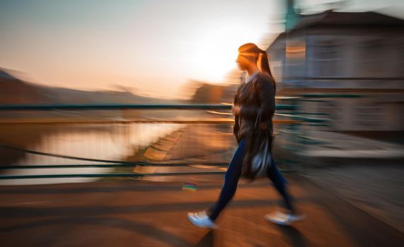 Abstract image of a woman walking down the street in morning sun light. Intentional motion blur