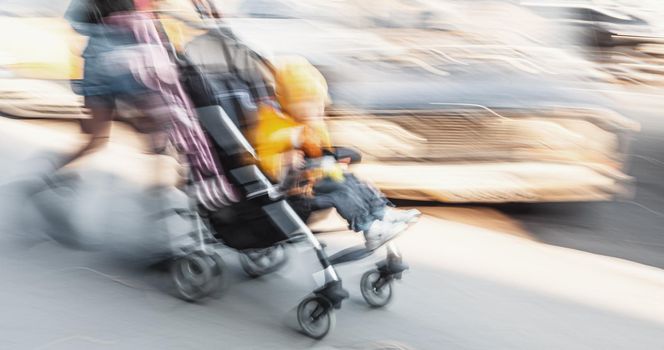 Mother with small child and a pram walking down the street. Intentional motion blur