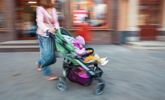 Mother with small child and a pram walking down the street. Intentional motion blur