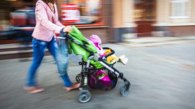 Mother with small child and a pram walking down the street. Intentional motion blur