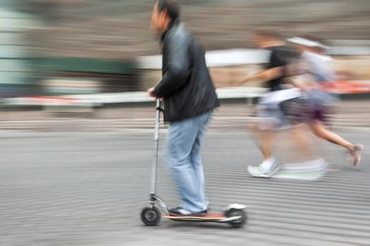 Man on a scooter and a pair running down the street. Intentional motion blur and color shift
