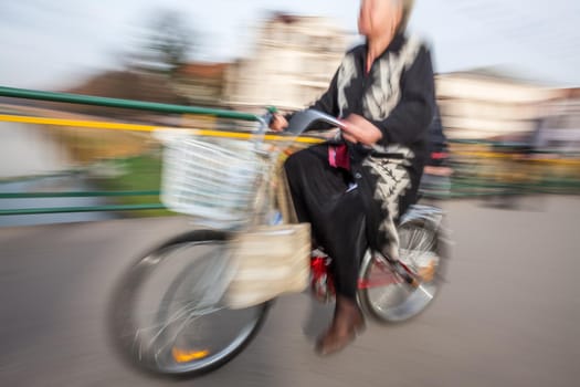 Old woman riding a bicycle around the city. Intentional motion blur
