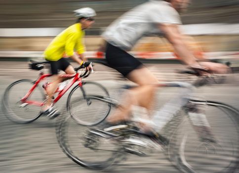 Two men ride bicycles on the streets of the big city. Intentional motion blur and color shift