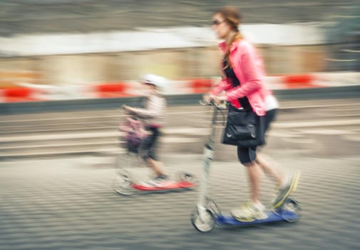 Young woman and boy riding on scooters. Intentional motion blur and color shift