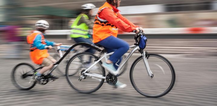 Young family with a child ride a bikes on a city streets. Intentional motion blur and color shift